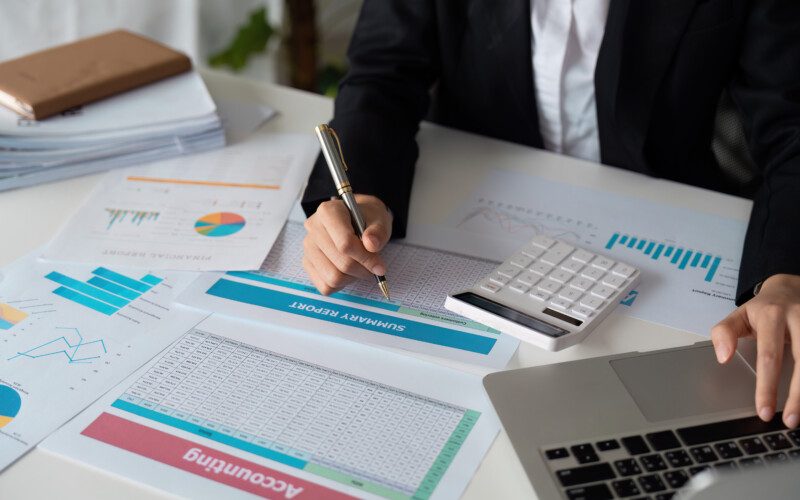 Business professional analyzing financial reports with a laptop, calculator, and charts in an office setting.